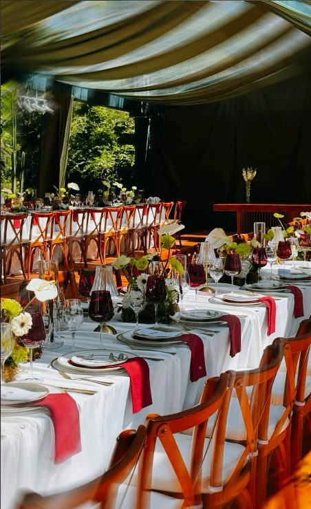 Mesa de convidados com guardanapos vermelhos, taças de vinho e cadeiras de madeira
